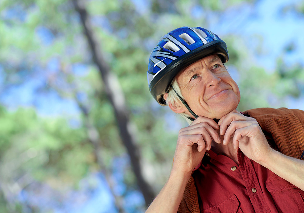 Nærbilde av en eldre mann sin er utendør i fint vær. Han har på seg en sykkelhjelm og justerer stroppen.