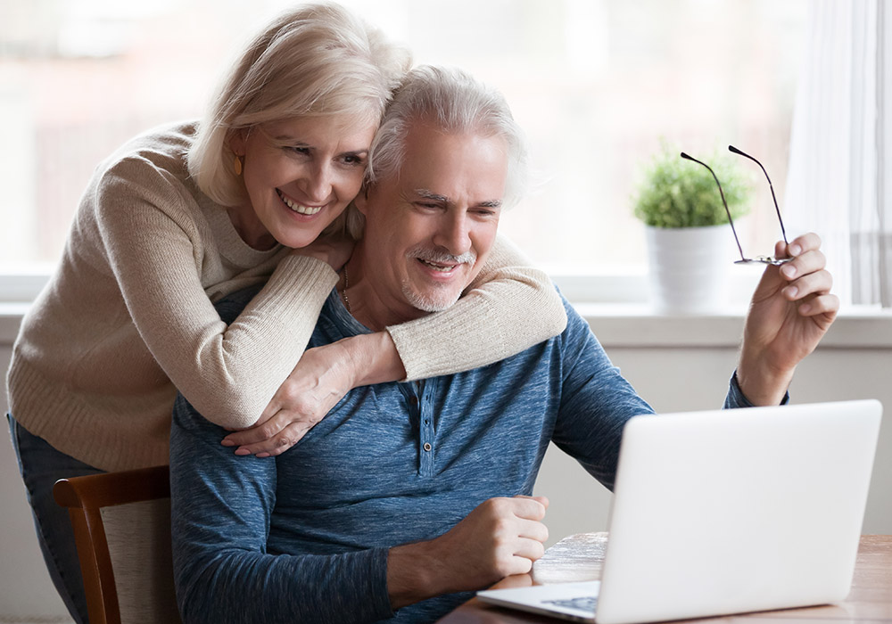 Et smilende eldre par som ser på en laptop sammen.