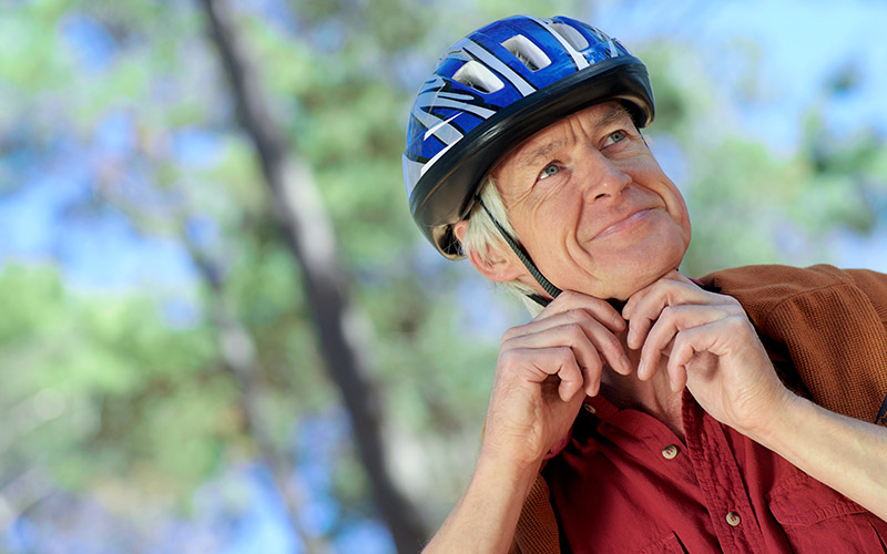 Vinklet nærbilde av en aktiv mannlig pensjonist, han justerer stroppene på sykkelhjelpen på hodet.
